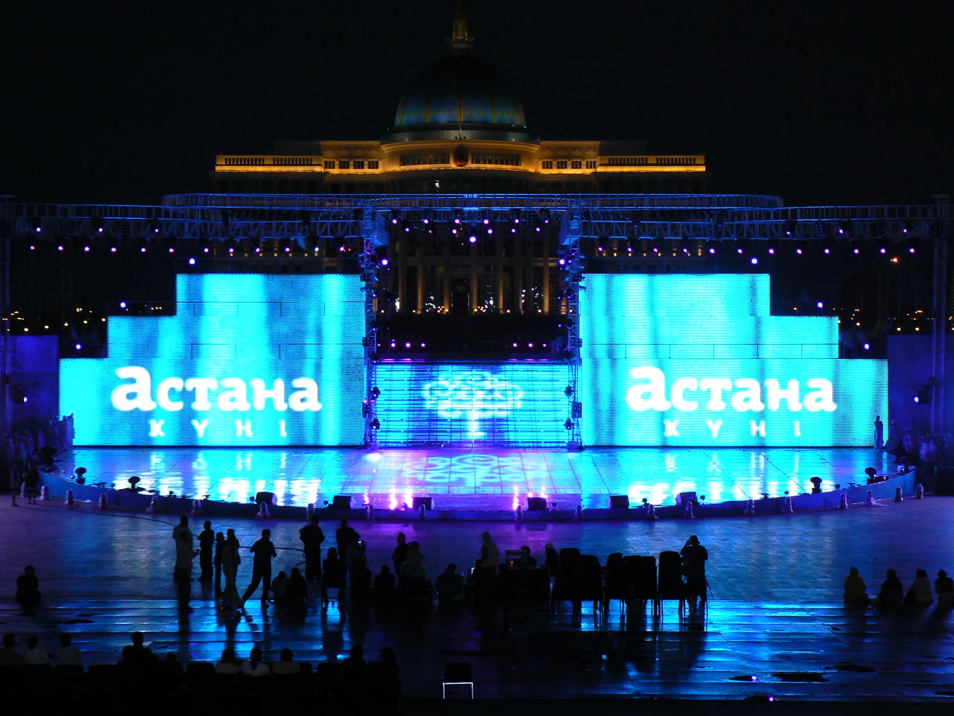 Ак Орда в золотой подсветке, перед ней две голубые LED-стены с надписью «Астана Күні»