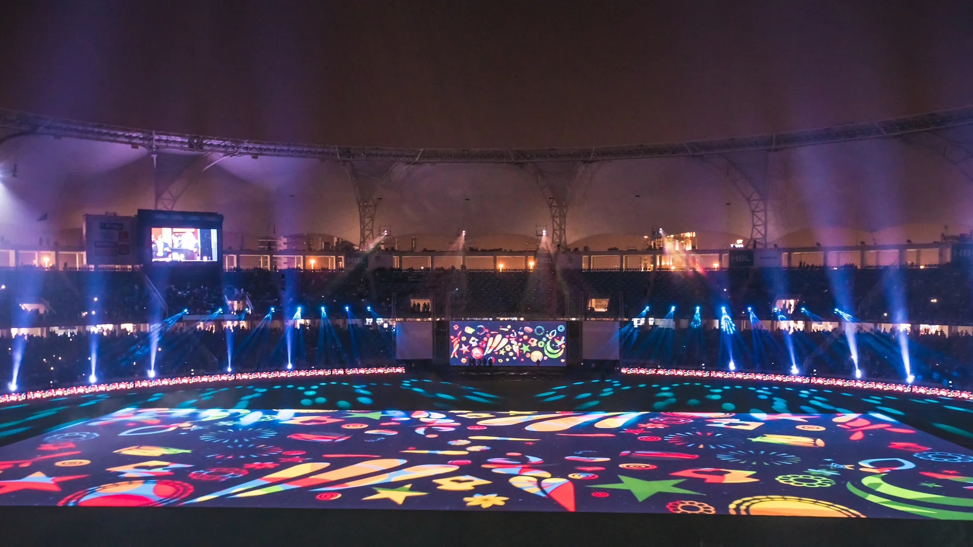 Стадион ночью: проекция цветных фигур на поле, лучи движущихся голов по периметру